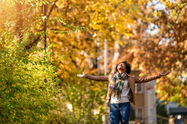 Happy mid adult African American woman enjoying a walk on autumn day in the park. Carefree tranquil woman with arms open day dreaming at the park.